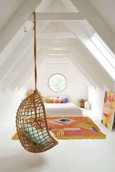 a bed sitting under a window in a bedroom next to a hanging chair and rug