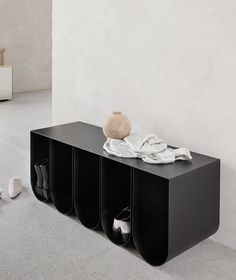 a black shelf with three pairs of shoes on it and a vase sitting on top