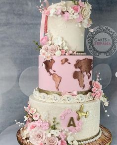 a three tiered cake with pink and white flowers on the top, topped with a world map