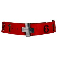 Norma Kamali Vintage Red Leather Novelty Cut Out Numbers Belt with Silver Cross Buckle S-M. Coral red leather belt with assorted cut out numbers, not sure if they mean anything, the numbers, that is. I've not seen another one, this from the 1990s. Attached silver metal cross buckle with a prong that works with the holes on the other end. Embossed stamp inside marked Norma Kamali S-M. In very good condition the cross buckle has a few light marks. Measurements are in inches: 32 1/2 from buckle hoo 2000 Belts, Red Belt Aesthetic, Red Gothic Fitted Corset Belt, Cross Buckle, Classic Red Belt Buckles With Removable Belt, Embossed Stamp, Vintage Givenchy, Chanel Runway, Wide Leather Belt