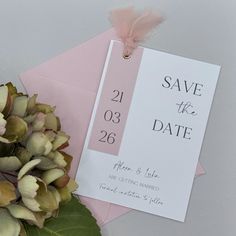 a pink and white save the date card next to flowers on top of an envelope