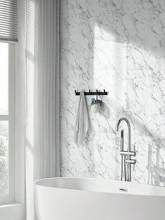 a white bathtub sitting next to a window in a bathroom with marble walls and floors