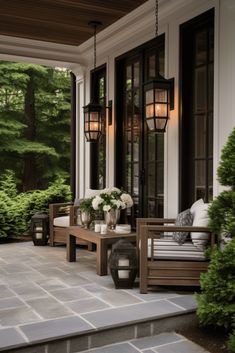 a porch with two benches and lanterns on the front door, surrounded by greenery