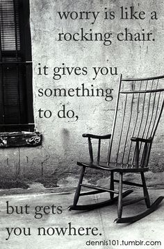 a wooden rocking chair sitting on top of a sidewalk next to a wall with a quote