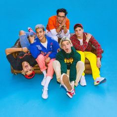 group of young men sitting on top of a wooden bench in front of a blue background