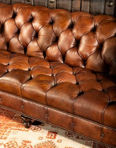 a brown leather couch sitting on top of a carpeted floor next to a wooden wall