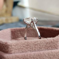 a diamond ring sitting on top of a pink velvet box with its reflection in it