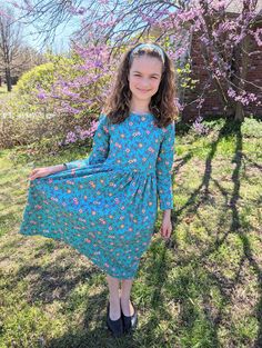 "Here is a simple and pretty long sleeve dress for girls. This classic style dress is made with 100% cotton fabric. It features a semi-fitted bodice, straight long sleeves, and a long gathered skirt. The fabric has a pretty teal background with medium size coral, yellow and other colored flowers scattered all over it. This simple, modest dress style makes a great play dress, but it is also nice enough to be worn for church, special occasions, or just about anywhere. It would make a great birthday gift for a special girl, or a nice addition to her wardrobe. This girls size 12 dress measures about 30 1/2\" around the chest and is 42\" long. All seams have been professionally finished with a serger. A matching fabric headband comes with the dress to add the finishing touch to the outfit. Than Fitted Long Sleeve Cotton Dress, Modest Long Sleeve Cotton Dress, Simple Modest Dress, Pretty Long Sleeve Dresses, Long Gathered Skirt, Modest Dress, Teal Background, Fabric Headbands, Colored Flowers