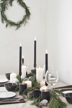 the table is set with black and white dishes, candles, pine cones, and evergreen garland