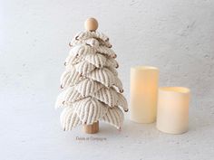 a small white knitted christmas tree next to a lit candle on a table with a white wall in the background