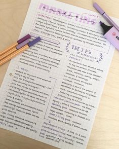 two pencils sitting on top of a piece of paper next to some writing utensils