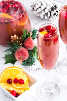 two wine glasses filled with fruit punch and garnished with pineapples, cranberries, and orange slices