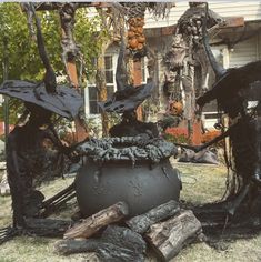 two black statues sitting in the grass next to a large pot filled with firewood