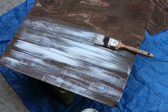 a paintbrush sitting on top of a wooden table next to a blue tarp