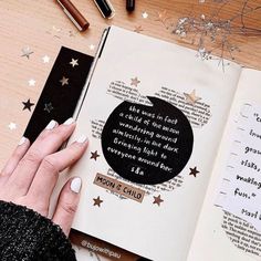 a woman's hand is holding an open book with writing on it and surrounded by stars