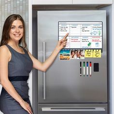 a woman is pointing at a magnetic board on the refrigerator's door while standing in front of it