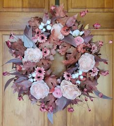 a wreath with pink flowers and leaves hanging on a wooden door frame in front of a wood paneled door