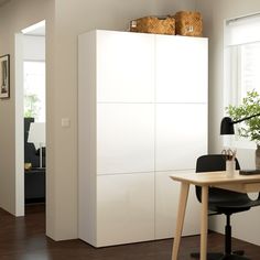 a room with a desk, chair and white cupboards in it's center