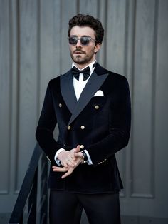 a man in a tuxedo and sunglasses poses for the camera with his hands on his hips