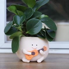 a potted plant with a smiling face holding a ukulele