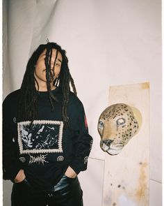 a man with dreadlocks standing next to a fake leopard head on a wall