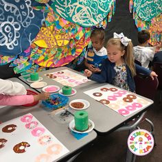 children are sitting at a table making doughnuts