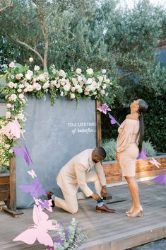 a man and woman standing next to each other in front of a flower covered wall