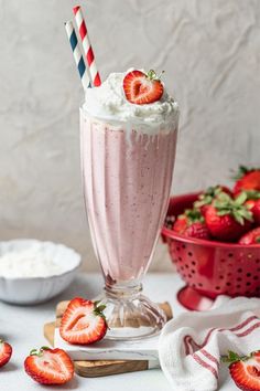 a strawberry milkshake with whipped cream and strawberries on the table next to it