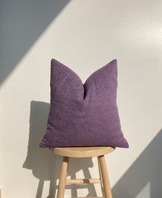 a purple pillow sitting on top of a wooden stool in front of a white wall