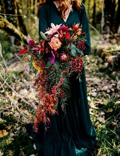 a woman wearing a green dress holding a bouquet of flowers in her hands while standing in the woods