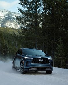 the infiniti suv is driving on snow - covered road with trees and mountains in the background