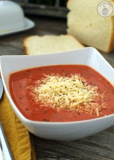 a bowl of tomato soup with parmesan cheese on top and bread in the background