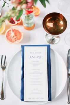 a white plate topped with a menu next to silverware and oranges on top of a table