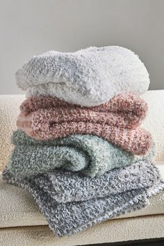 towels stacked on top of each other in different colors and sizes, sitting on a couch