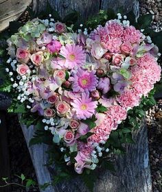 a heart - shaped arrangement of pink and white flowers on a wooden post in the sun