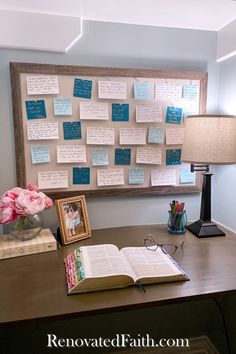 an open book sitting on top of a wooden desk next to a lamp and flowers