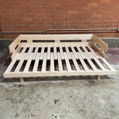 a wooden bed frame sitting in front of a brick wall with no sheets on it