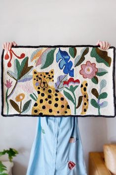 a person holding up a rug with a cat on it's face and flowers in the background