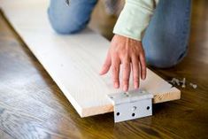 a person kneeling on the floor with their hand on top of a piece of wood