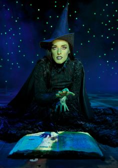 a woman dressed as a witch sitting in front of an open book on the ground