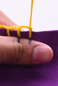 a person is stitching with yellow thread on a purple piece of cloth that they are holding in their left hand