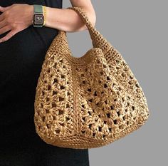 a woman is holding a crocheted handbag in her right arm and wearing a watch on her left wrist