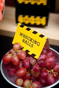 a bowl filled with grapes sitting on top of a table next to a sign that says wrecking balls