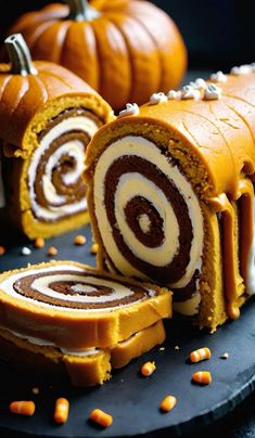 pumpkin roll with chocolate and white frosting on a black plate next to small pumpkins