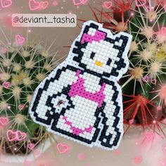 a cross stitch hello kitty ornament hanging from a cactus with pink flowers in the background