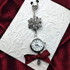 This delightfully whimsical, and fully functional, vintage style watch adds a touch of classic Victorian flair to your chatelaine! This stunning watch features many intricate details like the large floral filigree ornament, scrolled watch hands, and antique silver drop ornament that add so much elegance and charm. It also has a large vintage style clasp, so it can be easily attached or removed from your chatelaine.   The watch comes with the battery installed, just remove the white plastic guard on the side knob, turn the knob clockwise to set the time, and then push the knob in to activate the watch.   SIZING/ MEASUREMENTS   Watch face: 1 inch diameter Total length: 5 inches **Made in a smoke/pet free environment** SHOP POLICIES CANCELLATION: You can request cancellation within 24 hours o Metal Pocket Watch With Round Dial For Gift, Metal Pocket Watch With Round Dial As Gift, Metal Pocket Watch With Round Dial, Metal Watch Accessories With Round Dial For Gift, Metal Round Watch Accessories For Gift, Vintage Silver Watches With Compass Design, Handmade Elegant Formal Watches, Elegant Handmade Formal Watches, Antique Silver Watch Accessories Gift