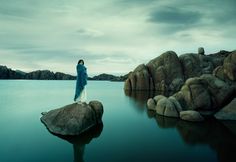 a woman standing on top of a rock in the middle of a body of water