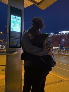 two people hugging each other in front of a bus stop with the city lights behind them