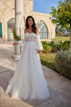 a woman in a white wedding dress standing on a stone walkway with her arms out