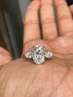 a person's hand holding an engagement ring with three pear shaped diamonds